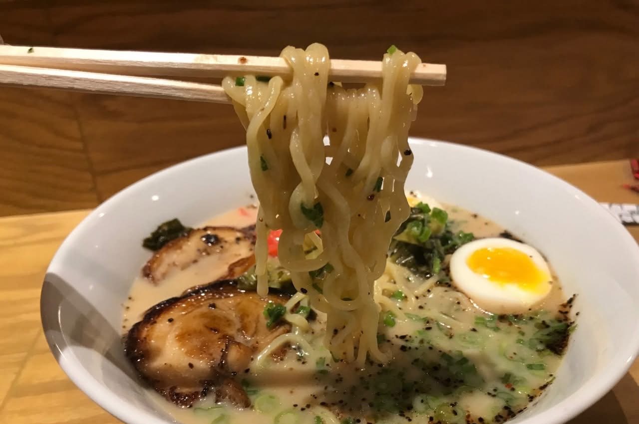 Ramen noodles lifted with chopsticks over a bowl of tonkotsu ramen with chashu pork and a soft egg at Mix Pacific Rim