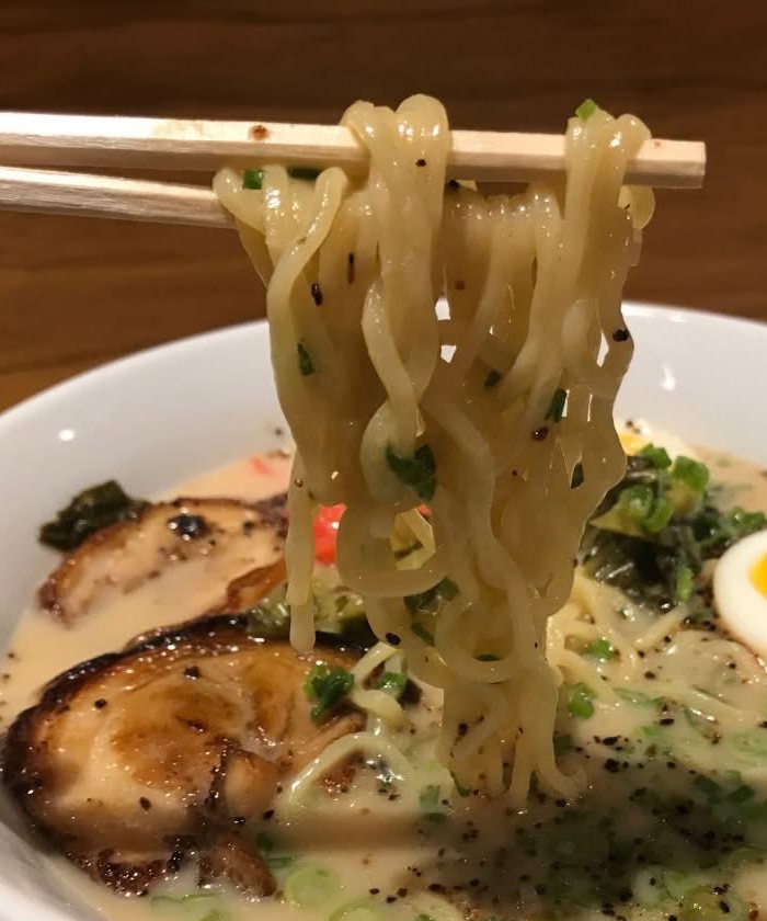 Ramen noodles lifted with chopsticks over a bowl of tonkotsu ramen with chashu pork and a soft egg at Mix Pacific Rim